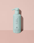 Fenty Hair The Rich One Moisture Repair Conditioner aluminum bottle with a pump on a pink background.